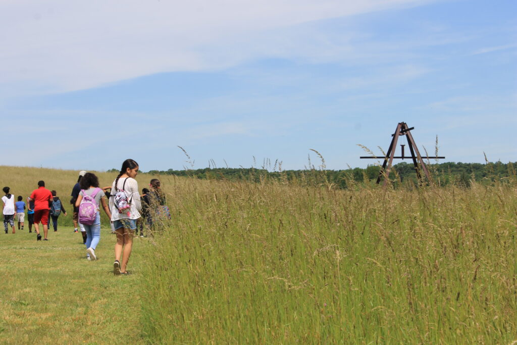 Kids walking outside on a sunny day in grassy field with a large sculpture in the distance