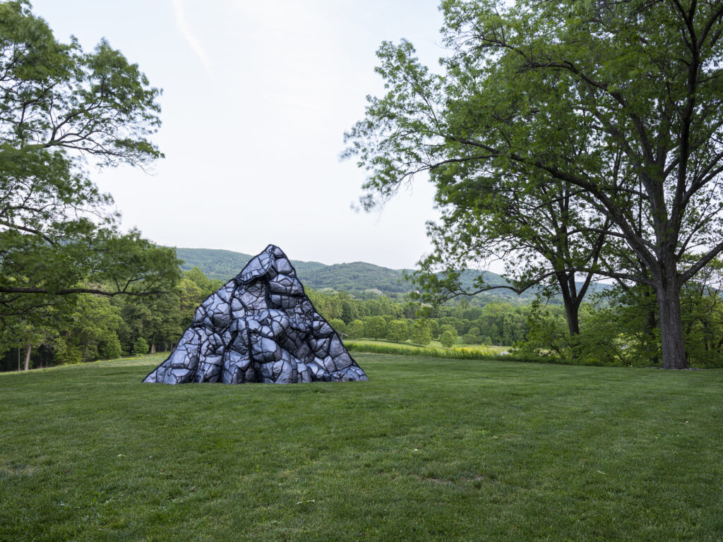 steel sculpture evoking a volcano, set against green meadows and trees 