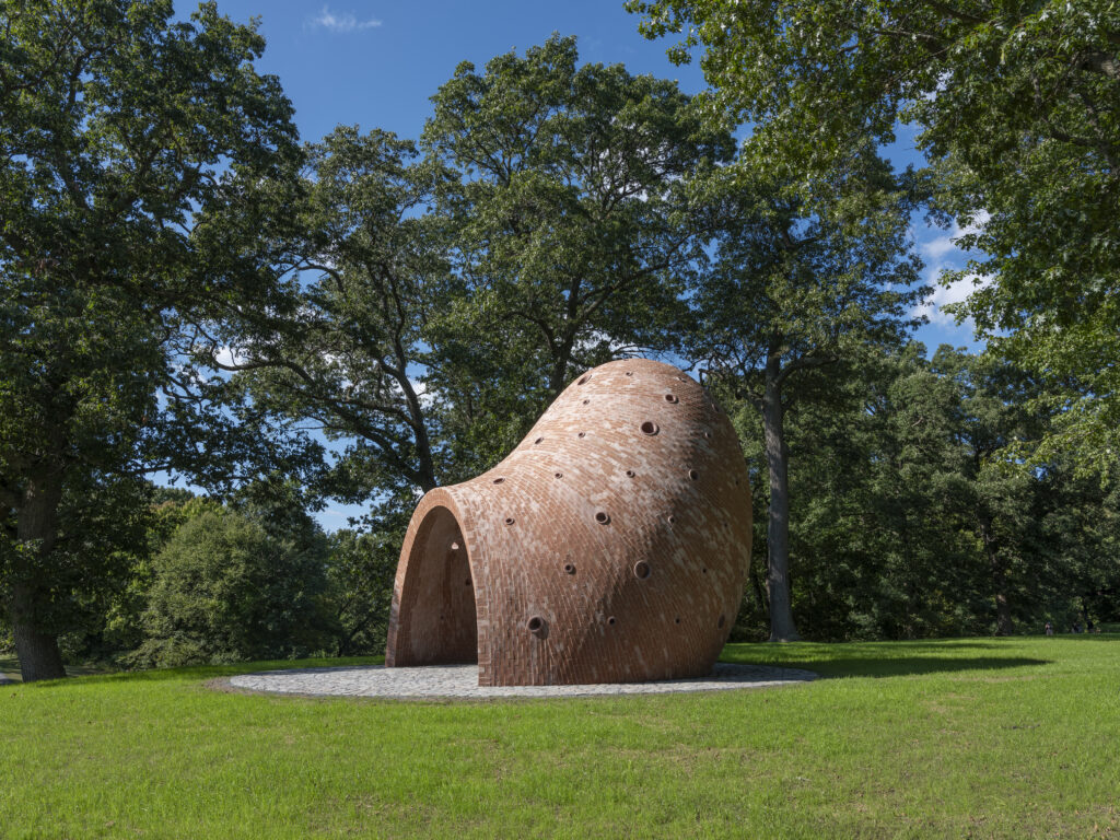 dome-shaped brick sculpture shown in profile against green grass and trees