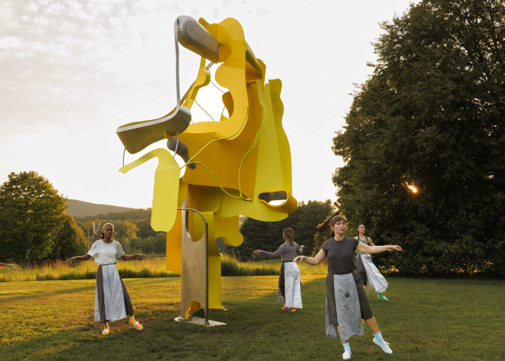 dancers surround a tall yellow sculpture at sunset