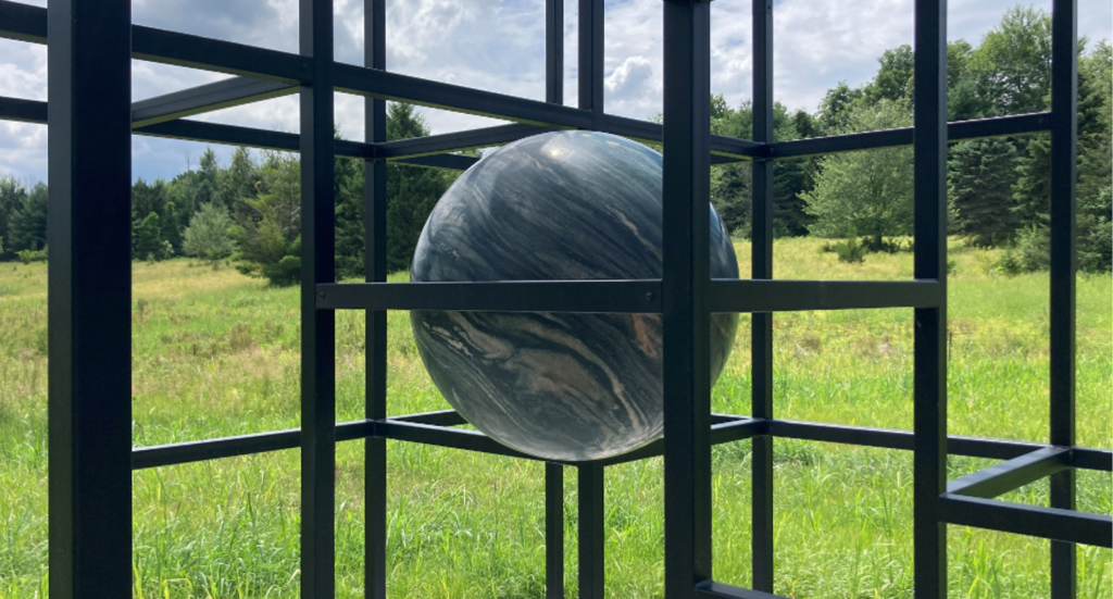 a three dimensional grid of black steel cubes with large spherical stones suspended