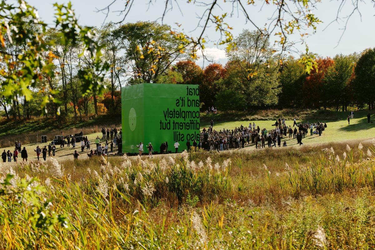 a 30-foot sculptural replica of charli xcx's brat remix album, black text on green vinyl. installed in storm king's landscape and surrounded by people. 