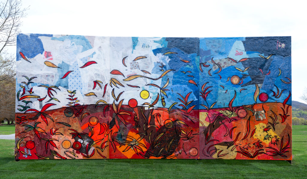 a tall rectangular panel standing on grass, consisting of an autumnal landscape,