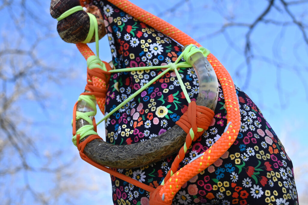 A closeup of a colorfully patterned sculpture, adorned with floral textiles and rope.
