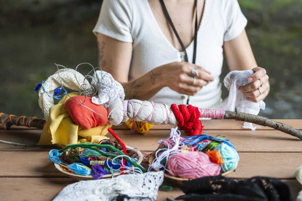 A person is crafting a sculpture from vibrant textiles and branches on a picnic table.