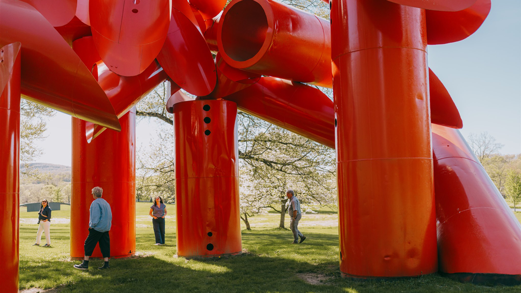 A close up look at Alexander Liberman's bright red sculpture Iliad. Four people stand under the sculpture.