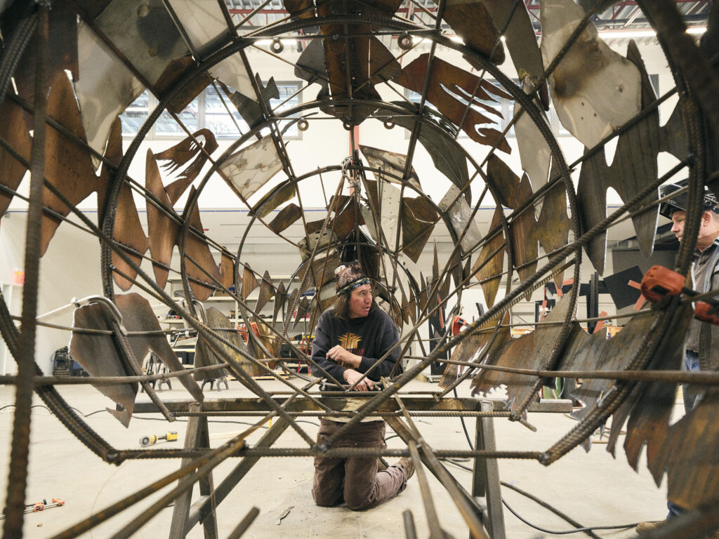 Artist Saif Azzuz sits at the center of a tube shaped sculpture that is covered with artistically carved sheets of metal.