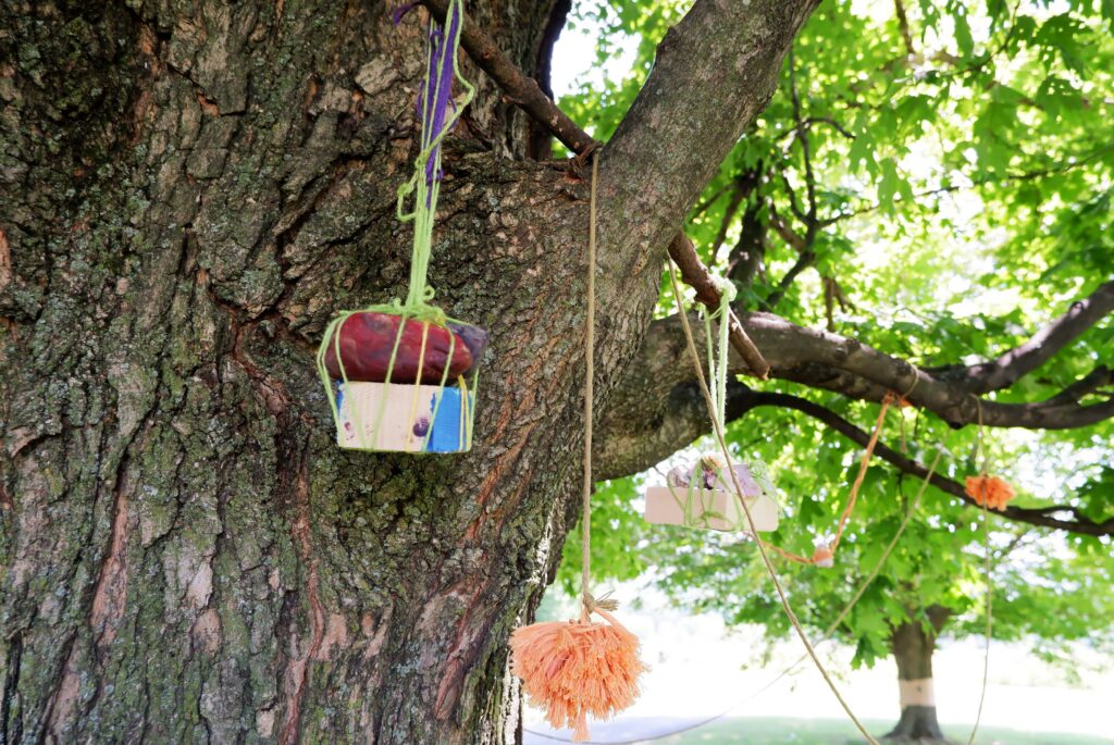 Objects made from natural material such as wood wrapped in string hang from a tree.