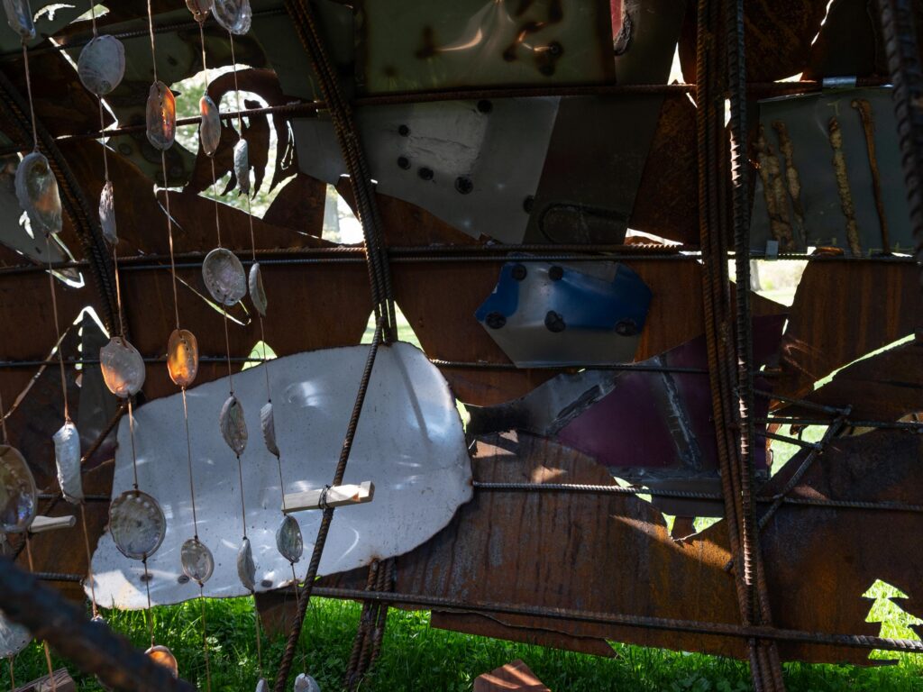 The inside of a life-size metal sculpture showing strings of shells vertically hanging down.